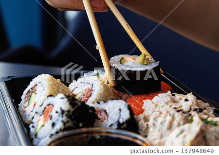 Chopsticks grasping sushi roll with cucumber, avocade and salmon. Maki  being picked up with chopsticks.  Selective focus 137948649