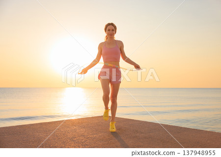 Fit woman jumping rope at the beach during summer vacation Fit woman jumping rope at the beach during summer vacation 137948955