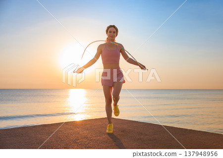 Fit woman jumping rope at the beach during summer vacation Fit woman jumping rope at the beach during summer vacation 137948956
