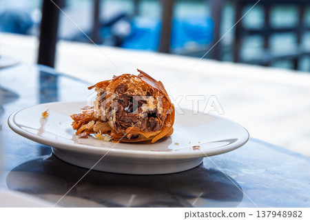 Closeup of the final bite of a traditional neapolitan sfogliatella pastry on a white ceramic plate on metallic table in outdoor cafe in italy. Selective focus 137948982