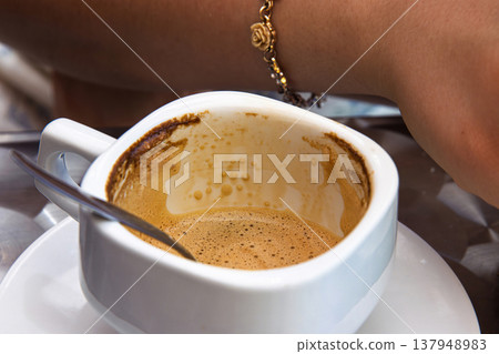 Finished espresso cup with coffee stains and spoon on a metal cafe table. Young woman arm  in the background. Selective focus 137948983