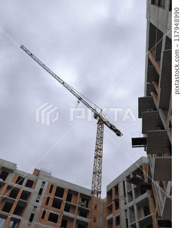 Construction site of a multi-story building, a towering crane against a backdrop of clouds 137948990