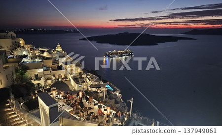Twilight view of Santorini illuminated cliffside village, with glowing terraces under a colorful sunset sky. Twilight view of Santorini illuminated cliffside village, with glowing terraces under a colorful sunset sky. 137949061
