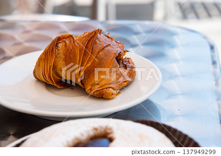 A traditional sfogliatella pastry on a white ceramic plate atop a shiny metallic table in outdoor cafe in Italy A traditional sfogliatella pastry on a white ceramic plate atop a shiny metallic table in outdoor cafe in Italy 137949299
