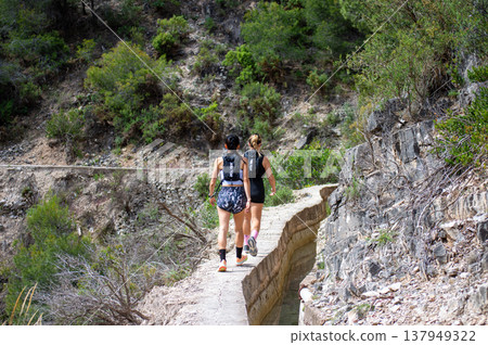 Scenic view of surrounding mountains and picturesque village from a hiking trail along an old irrigation ditch in Frigiliana, Spain. Scenic view of surrounding mountains and picturesque village from a hiking trail along an old irrigation ditch in Frigiliana, Spain. 137949322