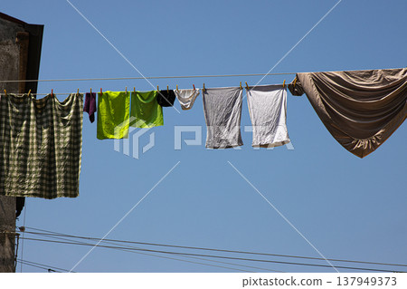 Colorful laundry drying on cloth lines in traditional Italian way. Ropes stretched between old buildings under a clear blue sky on a sunny day in Murano Colorful laundry drying on cloth lines in traditional Italian way. Ropes stretched between old buildings under a clear blue sky on a sunny day in Murano 137949373