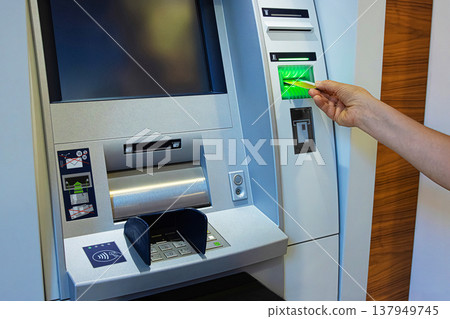 A person inserts a bank card into an ATM slot, initiating a secure banking transaction. Closeup of a client hand inserting a card into an cash machine terminal for money withdrawal 137949745
