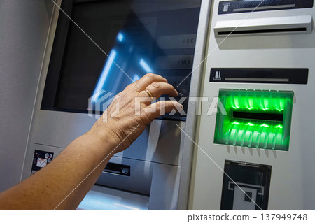 Person operating ATM touchscreen. The interface includes a card reader with glowing green lights and German language labels. Person operating ATM touchscreen. The interface includes a card reader with glowing green lights and German language labels. 137949748