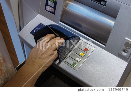 Person using the keypad of an ATM to enter information or PIN for a secure transaction. Closeup of a hand over keypad pressing buttons 137949749