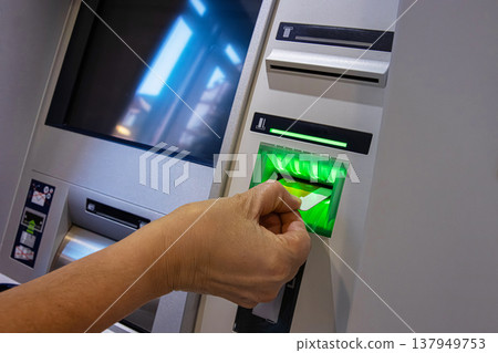 ATM Card Entering Illuminated Slot. Cash machine card reader slot glowing green as a card is inserted by person hand. 137949753