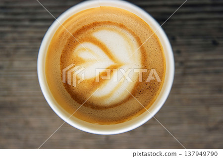 Top down view of a paper coffee cup, placed on a rustic wooden table, filled with a creamy latte featuring heart and flower shaped latte art Top down view of a paper coffee cup, placed on a rustic wooden table, filled with a creamy latte featuring heart and flower shaped latte art 137949790