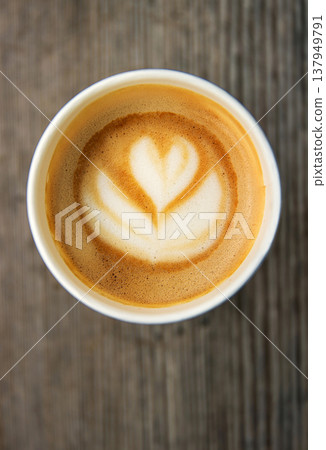 Top down view of a paper coffee cup, placed on a rustic wooden table, filled with a creamy latte featuring heart and flower shaped latte art Top down view of a paper coffee cup, placed on a rustic wooden table, filled with a creamy latte featuring heart and flower shaped latte art 137949791