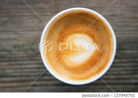 Top down view of a paper coffee cup, placed on a rustic wooden table, filled with a creamy latte featuring heart shaped latte art Top down view of a paper coffee cup, placed on a rustic wooden table, filled with a creamy latte featuring heart shaped latte art 137949793