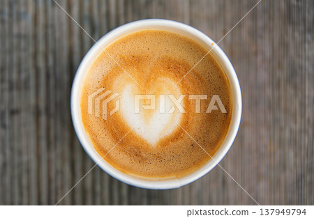Top down view of a paper coffee cup, placed on a rustic wooden table, filled with a creamy latte featuring heart shaped latte art Top down view of a paper coffee cup, placed on a rustic wooden table, filled with a creamy latte featuring heart shaped latte art 137949794