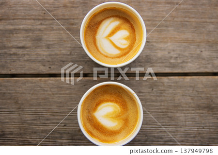 Top down view of two paper coffee cups, placed on a rustic wooden table, with a creamy heart and flower shaped latte art Top down view of two paper coffee cups, placed on a rustic wooden table, with a creamy heart and flower shaped latte art 137949798