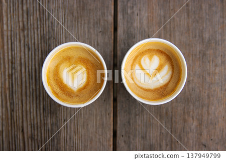 Top down view of two paper coffee cups, placed on a rustic wooden table, with a creamy heart and flower shaped latte art Top down view of two paper coffee cups, placed on a rustic wooden table, with a creamy heart and flower shaped latte art 137949799