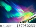 The night sky is filled with the aurora borealis, and the city is bathed in its glow at night. 137950233