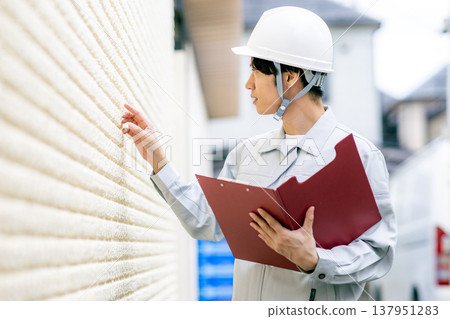 A man in work clothes inspects the exterior walls. A man in work clothes inspects the exterior walls. 137951283