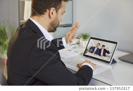 Video call on tablet, businessman greeting colleagues in online meeting session Video call on tablet, businessman greeting colleagues in online meeting session 137952817