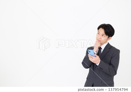 A middle-aged businessman thinking while looking at his smartphone. A middle-aged businessman thinking while looking at his smartphone. 137954794