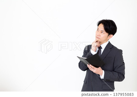 A middle-aged businessman carrying a black notebook, troubled by his worries. 137955083