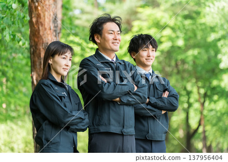 Male and female workers in forestry and civil engineering work clothes standing with their arms folded in the forest Male and female workers in forestry and civil engineering work clothes standing with their arms folded in the forest 137956404