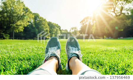 穿著運動鞋的雙腳坐在草地上，沐浴在公園裡清爽的陽光。 137956469