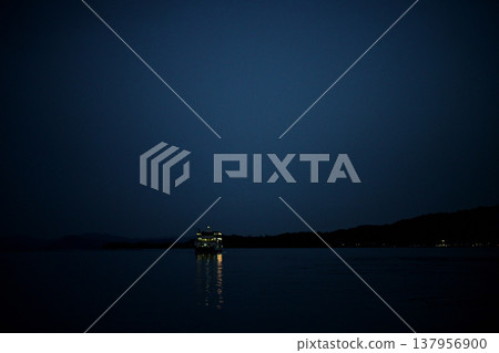 夜幕降臨,一艘小型觀光渡輪緩緩駛過寧靜的瀨戶內海。 夜幕降臨,一艘小型觀光渡輪緩緩駛過寧靜的瀨戶內海。 137956900