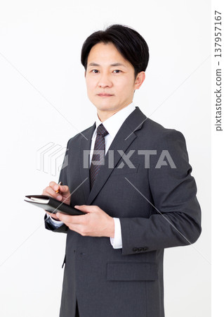 A middle-aged businessman carrying a black notebook. 137957167