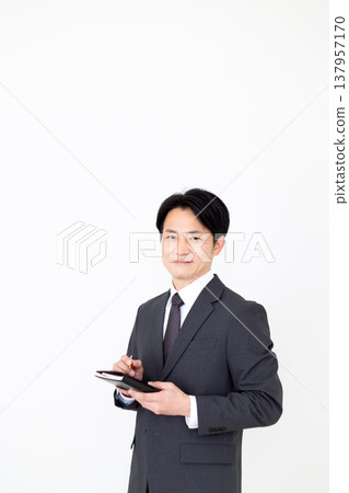一位中年商人,手裡拿著一本黑色筆記本。 一位中年商人,手裡拿著一本黑色筆記本。 137957170