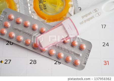 Pregnancy test with birth control pills and condom for female on calendar, ovulation day. 137958362