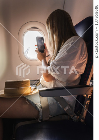 Young woman passenger photographing airplane wing view through cabin window Young woman passenger photographing airplane wing view through cabin window 137958686