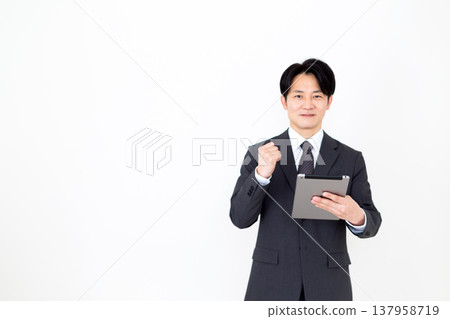 A middle-aged businessman makes a triumphant gesture while holding a tablet. A middle-aged businessman makes a triumphant gesture while holding a tablet. 137958719
