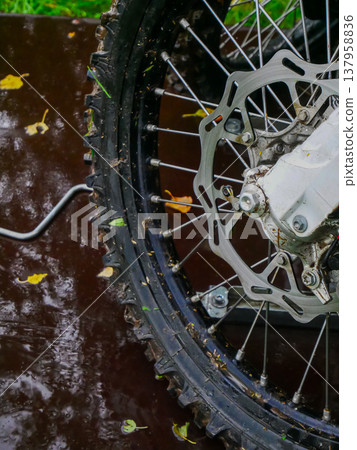 Dirty motorcycle wheel with treaded tire and steel brake disc on wet ground. Extreme motocross sport equipment. Off road motorbike part for competition and adventure hobby concept. Dirty motorcycle wheel with treaded tire and steel brake disc on wet ground. Extreme motocross sport equipment. Off road motorbike part for competition and adventure hobby concept. 137958836