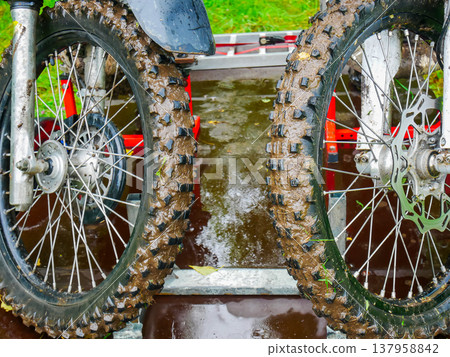 Muddy motorcycle tires on trailer. Extreme dirt bike wheels covered in thick mud after off road race. Dirty enduro motorbike equipment transportation. Adventure, sport and travel theme. Muddy motorcycle tires on trailer. Extreme dirt bike wheels covered in thick mud after off road race. Dirty enduro motorbike equipment transportation. Adventure, sport and travel theme. 137958842