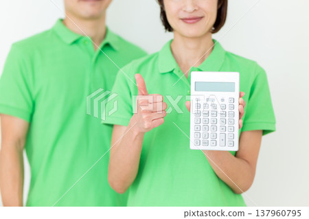 A middle-aged female care worker holding a calculator and giving a thumbs-up. A middle-aged female care worker holding a calculator and giving a thumbs-up. 137960795