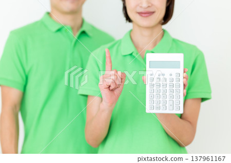 A middle-aged female care worker holding a calculator and raising her index finger. A middle-aged female care worker holding a calculator and raising her index finger. 137961167
