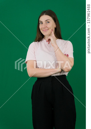 different emotions of a young girl on a green background chromakey beautiful facial features real people pink T-shirt white skinned European. black flared wide leg trousers 137961488