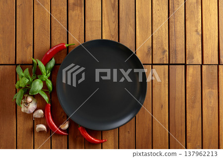 Empty black plate, garlic, basil, and red pepper on a natural wooden background. 137962213