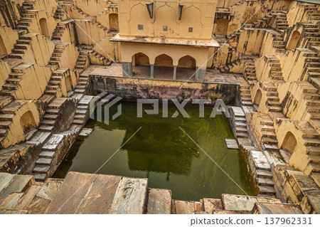 Old Indian stepwell with symmetrical stone stairs and murky green water. Old Indian stepwell with symmetrical stone stairs and murky green water. 137962331