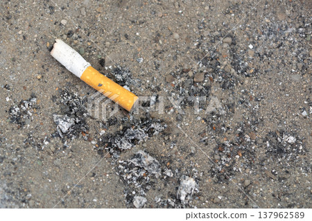 Close up of discarded cigarette butt on dirty ground with ash and debris representing pollution addiction waste and environmental neglect concept 137962589