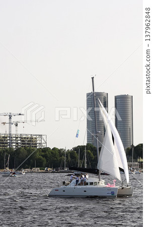 Riga, Latvia - June 30, 2024: A fleet of yachts moves with the wind along the shoreline. Riga, Latvia - June 30, 2024: A fleet of yachts moves with the wind along the shoreline. 137962848