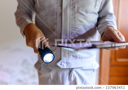 一名身穿工作服的男子拿著手電筒和文件。 一名身穿工作服的男子拿著手電筒和文件。 137963451