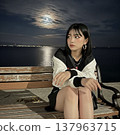 A high school girl sitting on a bench by the sea. 137963715