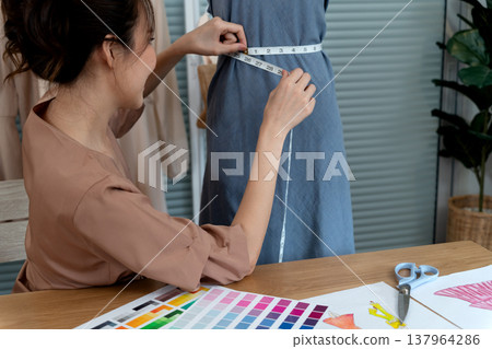 Yong woman designer is sizing a mannequin with a tape measure 137964286