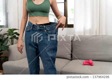young woman pulling her pants waist with her hand showing that she is thinner 137964296