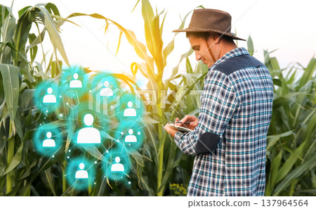 Farmer using a digital tablet in a corn field with a glowing social network or human resources icon. Concept of smart farming, agricultural management, and recruitment in agrotech 137964564