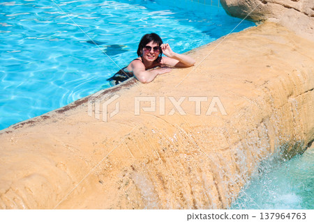 A woman swims in a pool with a waterfall 137964763