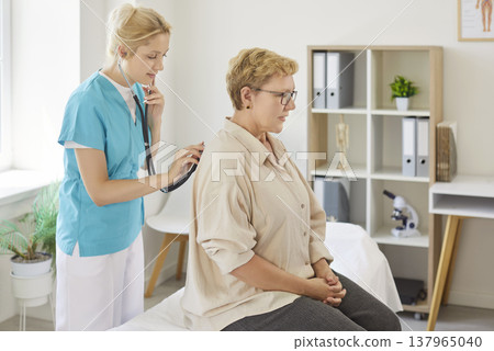Nurse using stethoscope to examine senior patient during medical clinic visit 137965040