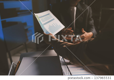 Two business people talk project strategy at office meeting room. Businessman discuss project planning with colleague at modern workplace while having conversation and advice on financial data report. Two business people talk project strategy at office meeting room. Businessman discuss project planning with colleague at modern workplace while having conversation and advice on financial data report. 137965531